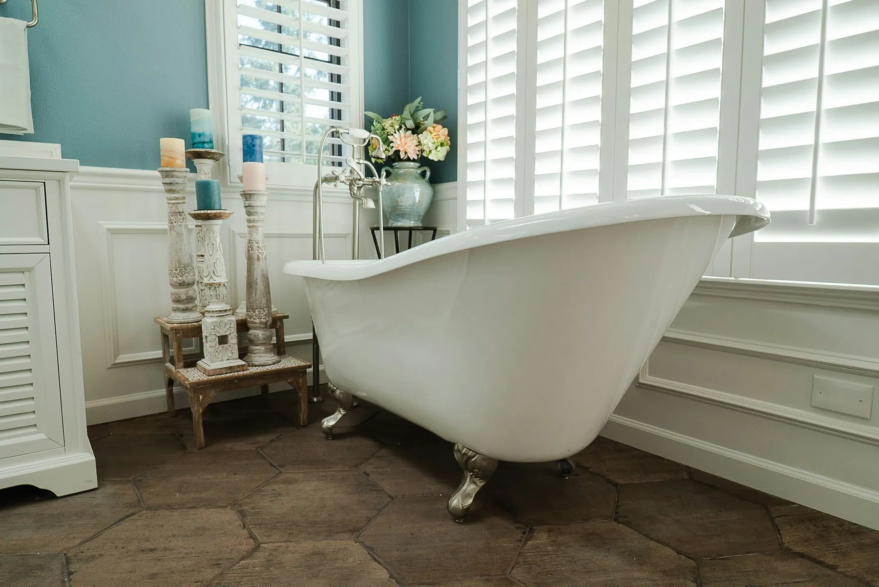 Classic clawfoot tub beside white plantation shutters and wainscoting