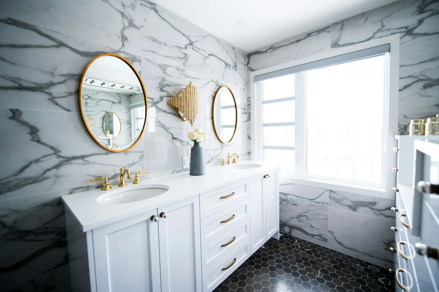 Marble-tiled bathroom with a white vanity, brass fixtures and round mirrors