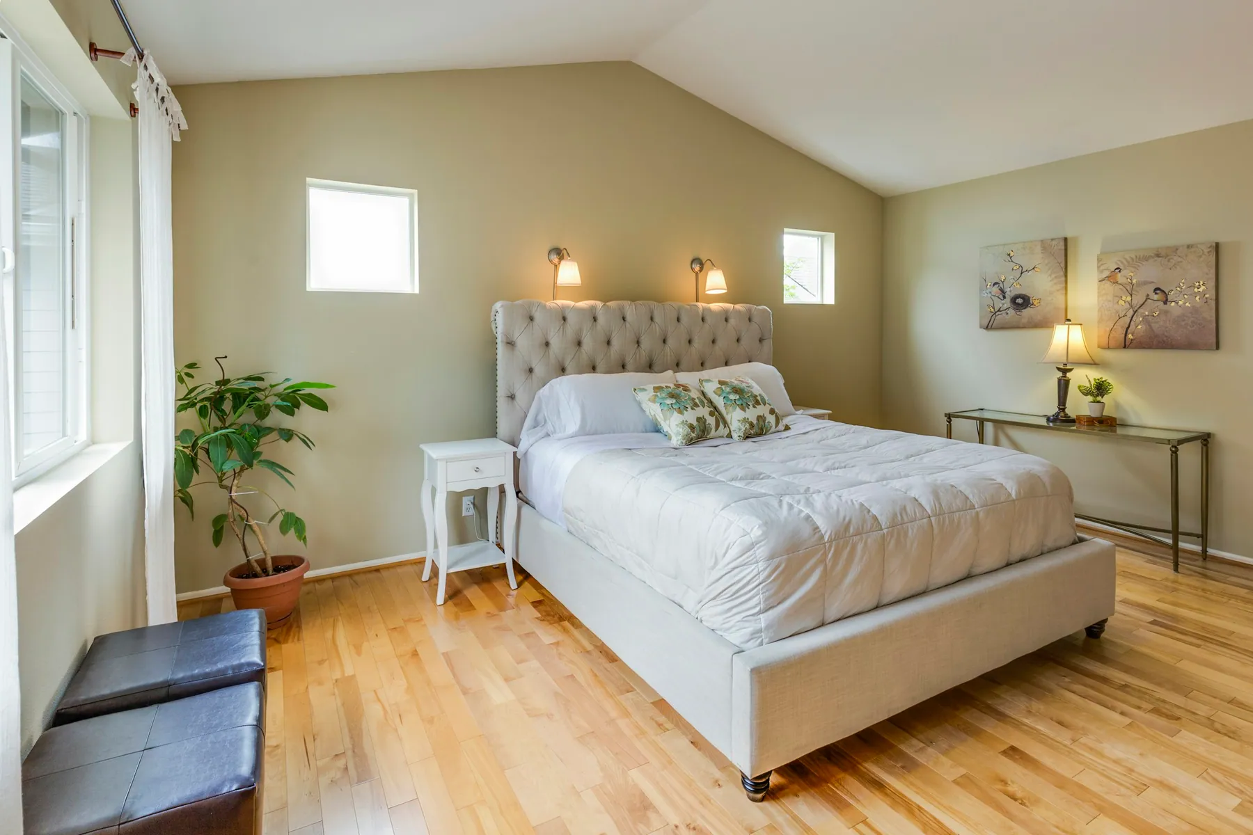 Vaulted bedroom with an upholstered bed and hardwood floor