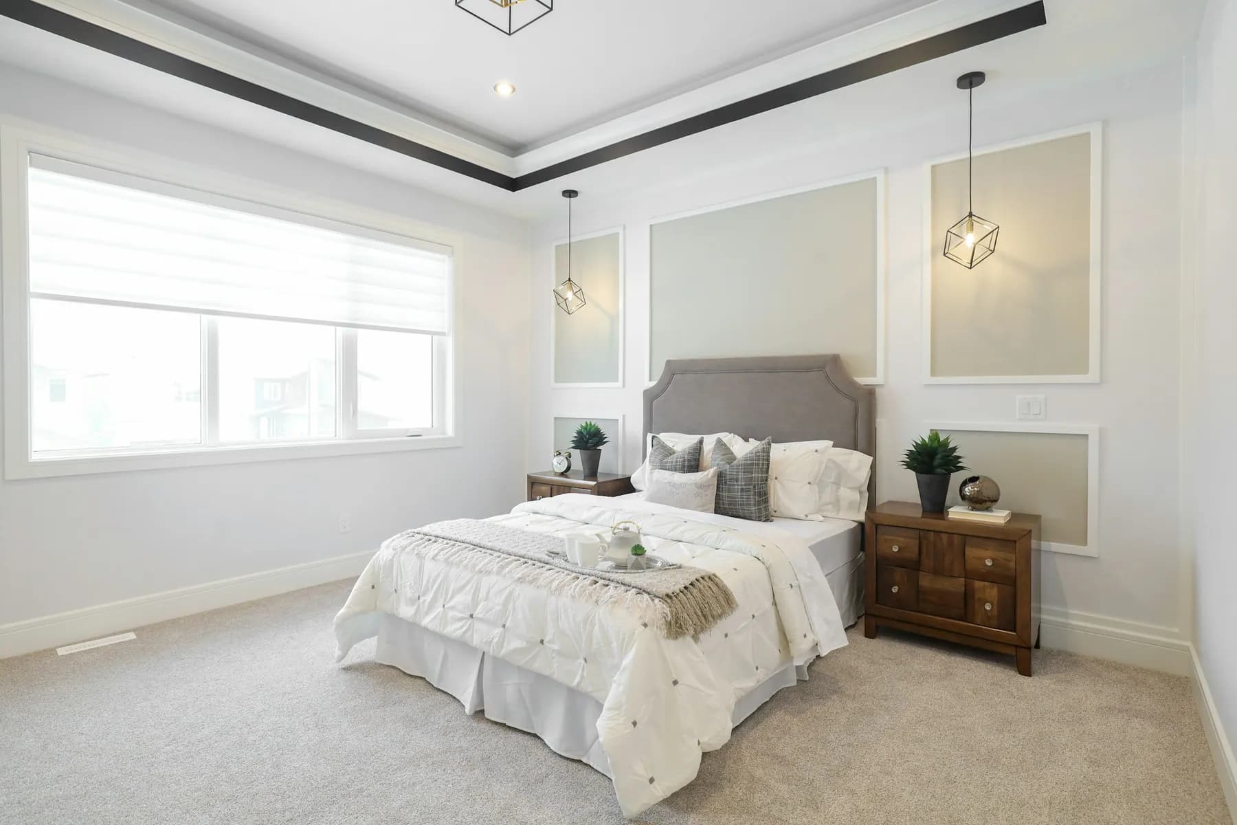 Bright carpeted bedroom with a tray ceiling and made bed