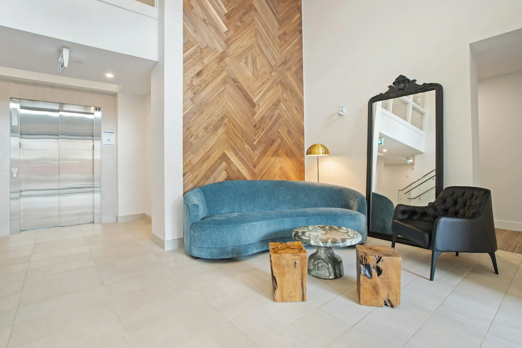 Building lobby with an elevator, a blue sofa and a herringbone wood wall