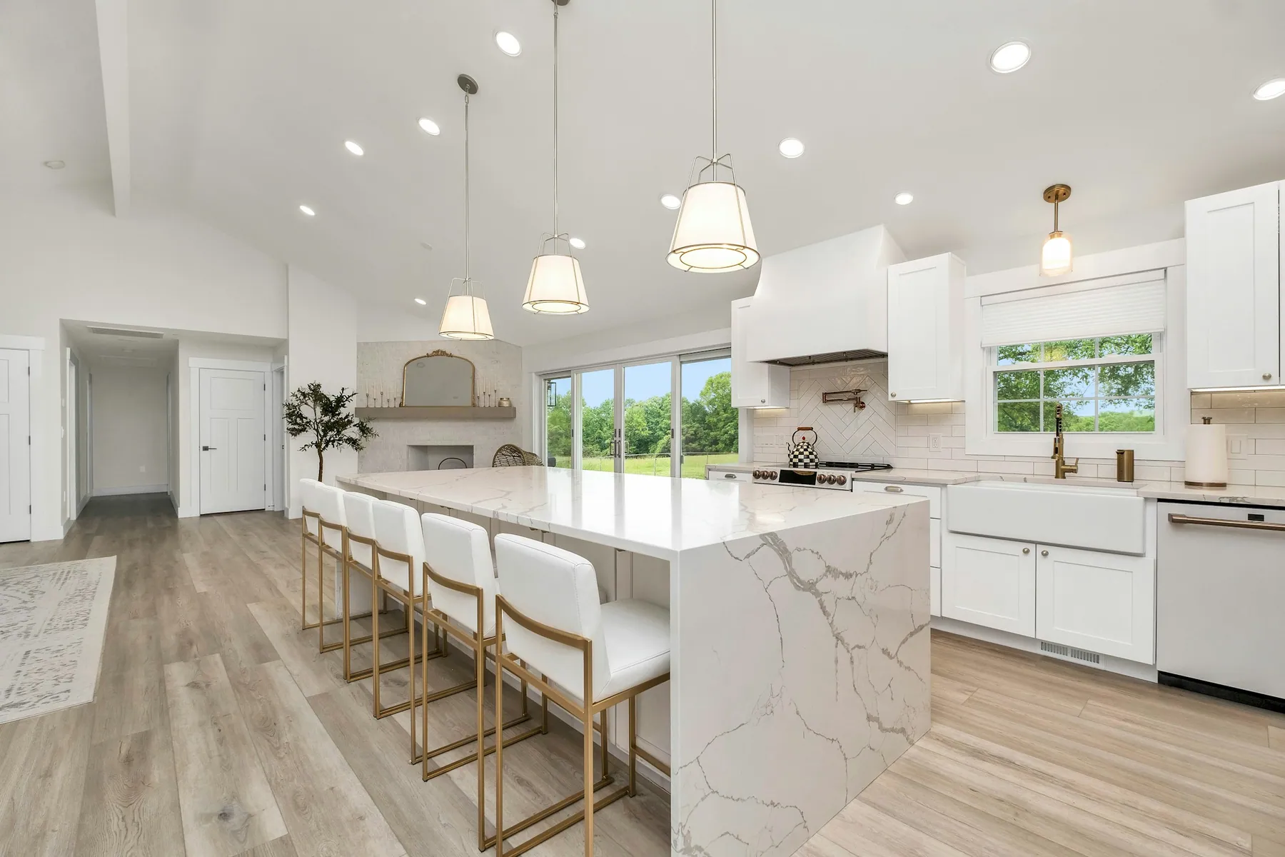 Open white kitchen with a marble waterfall island, bar stools and pendant lights