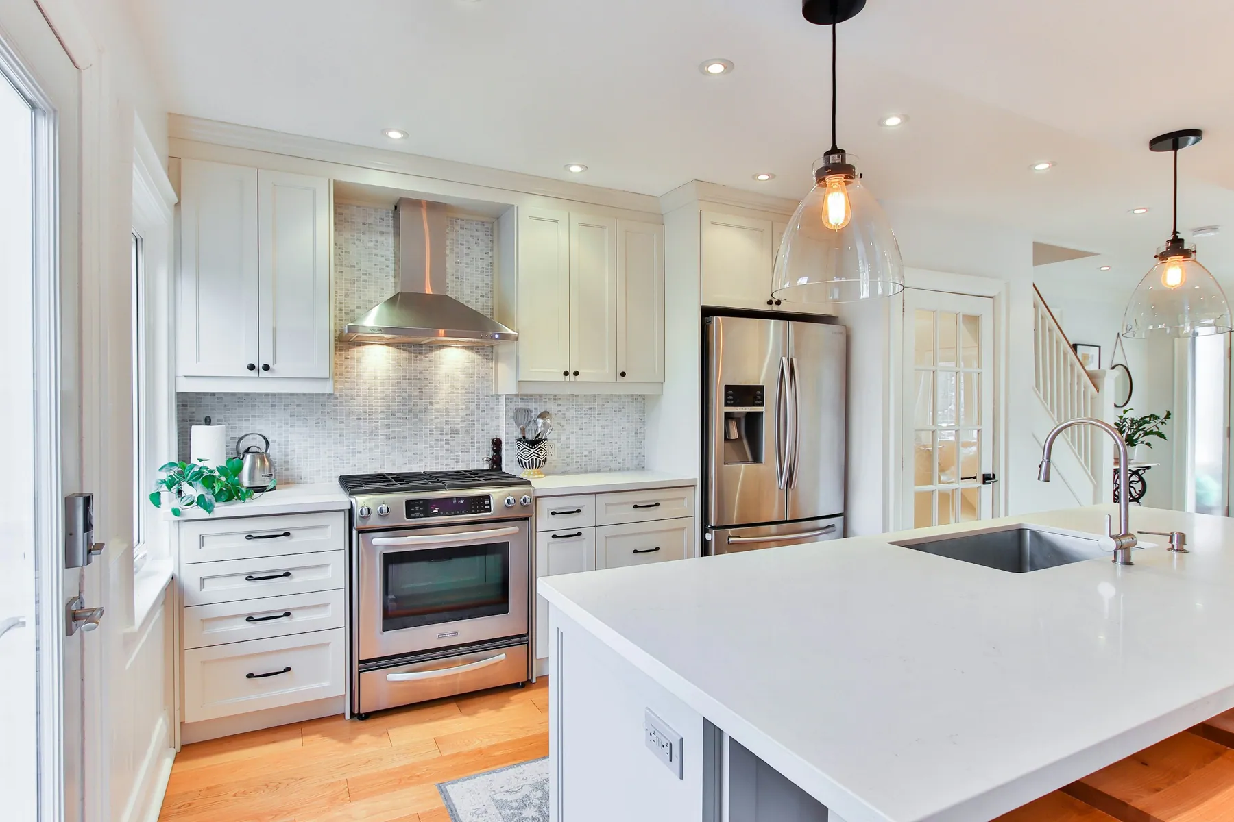 Bright white kitchen with stainless appliances, island sink and glass pendants