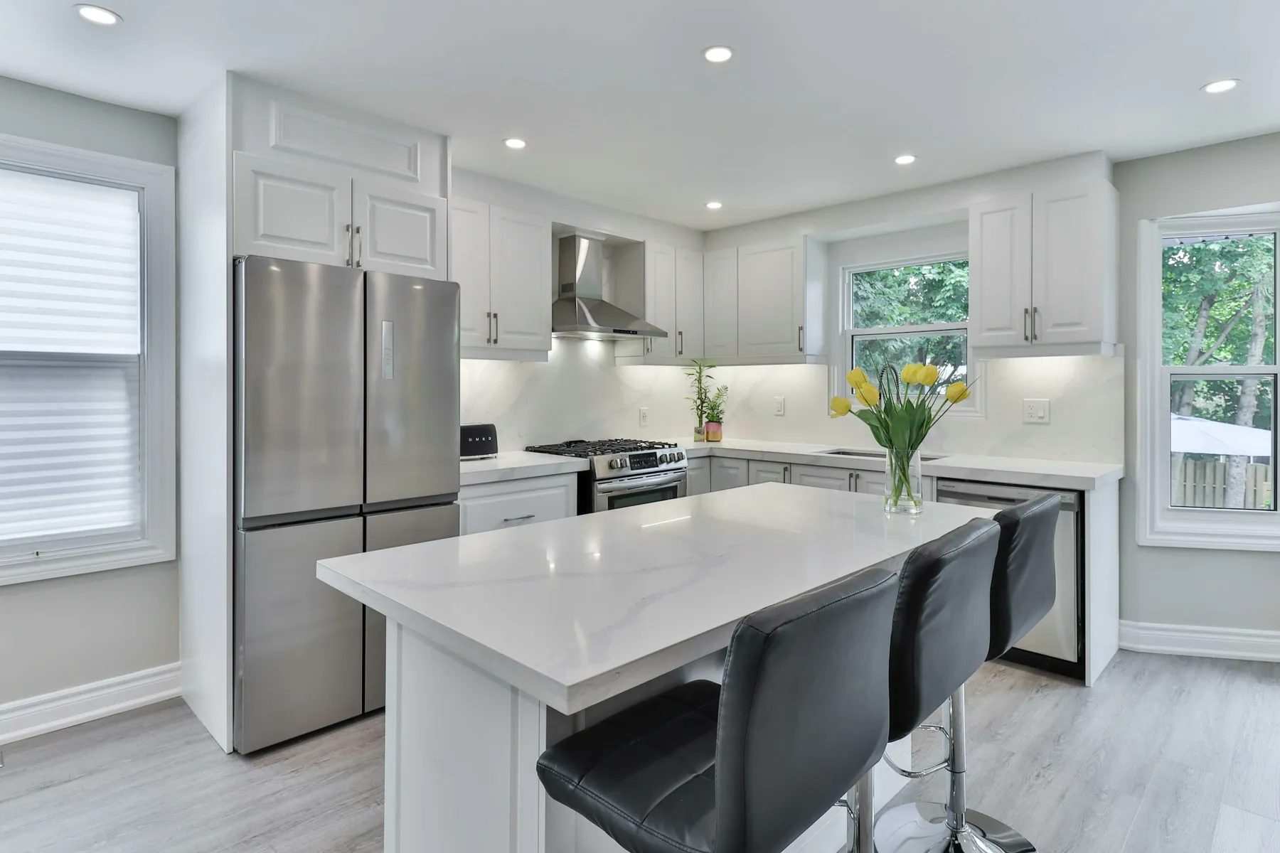 White kitchen with a stainless fridge, quartz island and leather stools