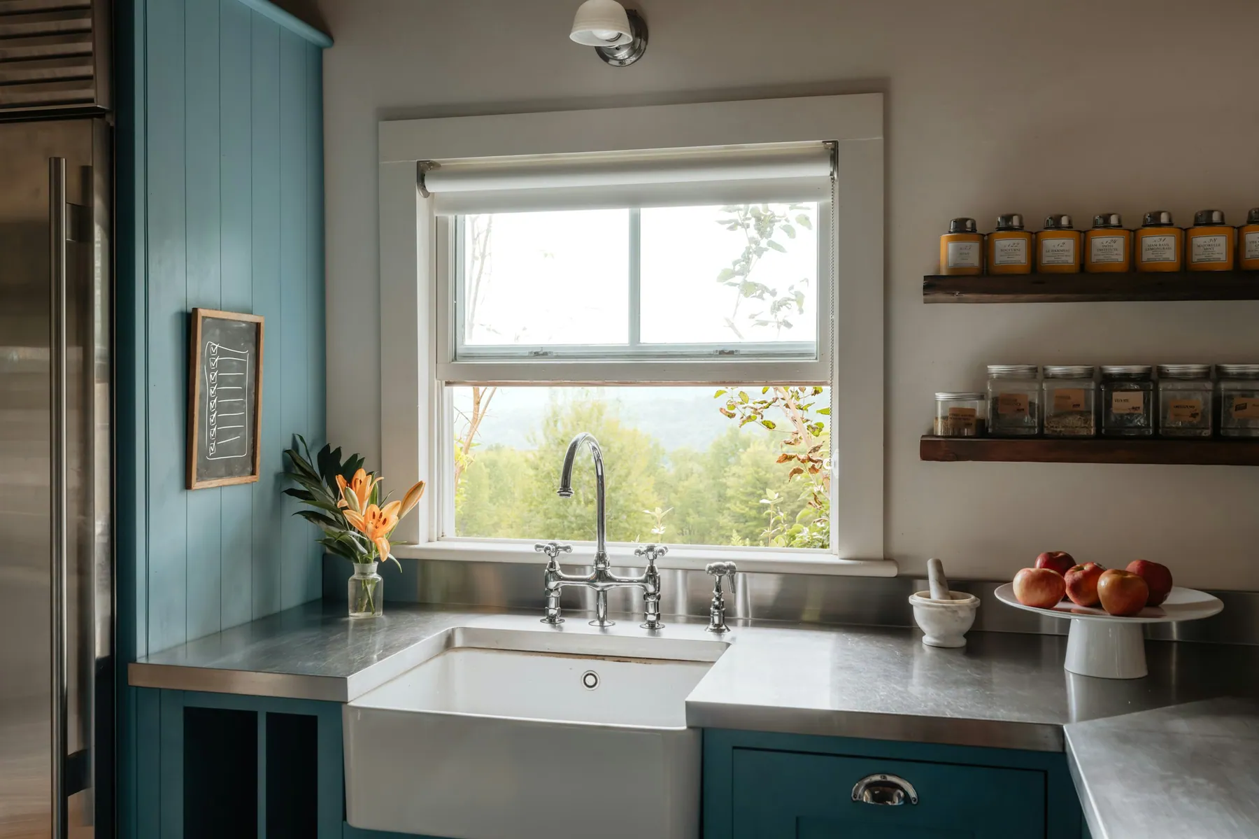 Farmhouse sink with stainless counters, teal cabinets and a garden window