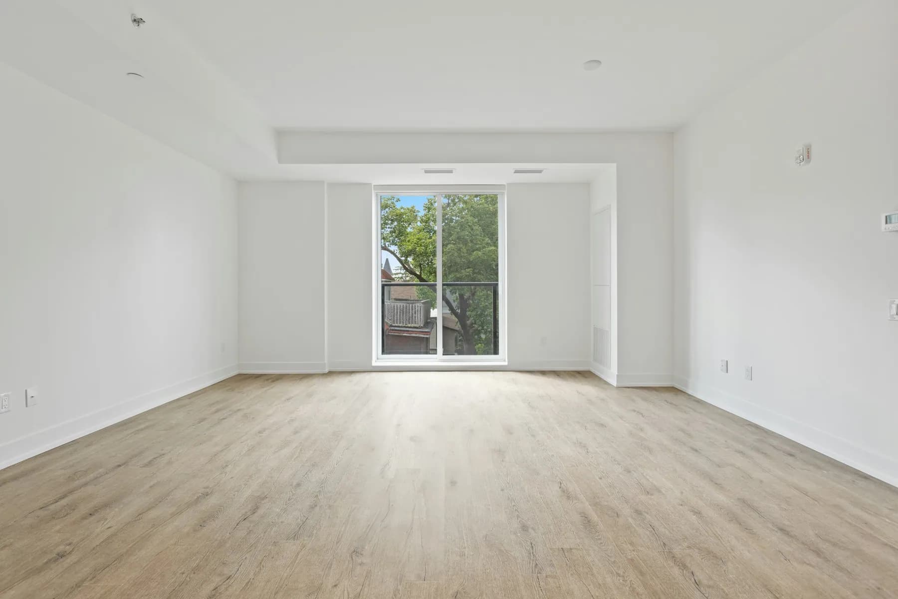 Empty apartment living room with a light plank floor and a balcony door